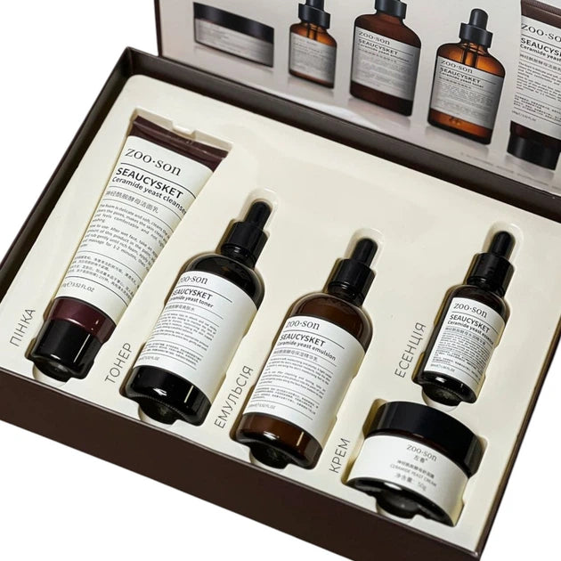 ZOO-SON facial care gift set in a brown box, containing a hand cream tube, three amber dropper bottles, and a jar, with a white insert showing additional product views.