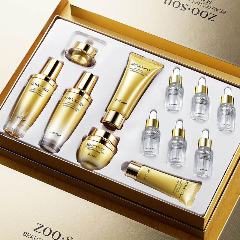 A boxed skincare set with multiple gold-toned bottles, tubes, and jars arranged inside an open presentation box. The products appear branded ZOO.