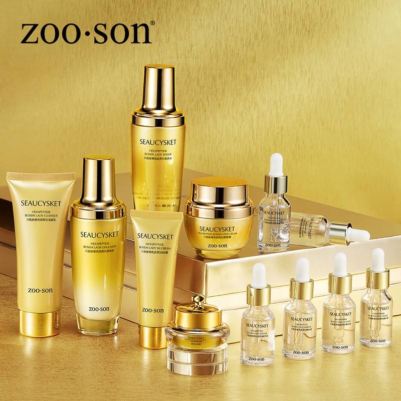A collection of ZOO-SON Sealucysket skincare products arranged on a metallic gold surface and platform. The set includes various bottles, jars, and tubes in gold and clear packaging with white and gold lettering.