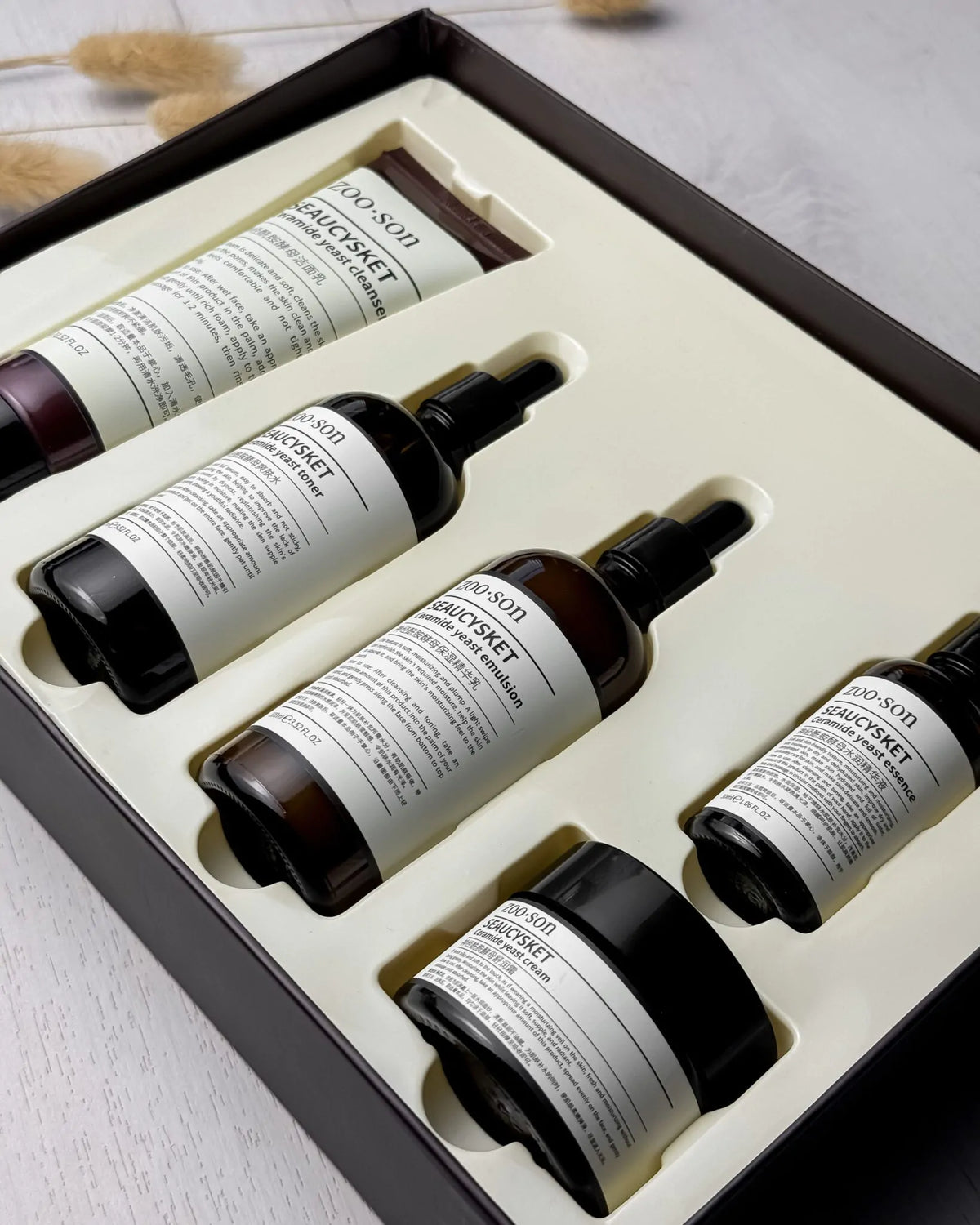 A boxed skincare set from ASOS, featuring a hand cream tube, three spray bottles, and a jar, arranged in a cream-colored foam insert inside a dark brown box.