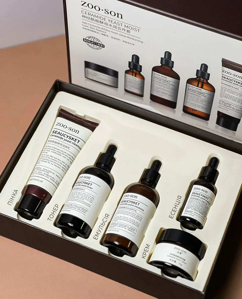 Zoo Son skincare gift set in an open presentation box, featuring a tube and four dropper bottles with amber glass and white labels, arranged on a beige surface.